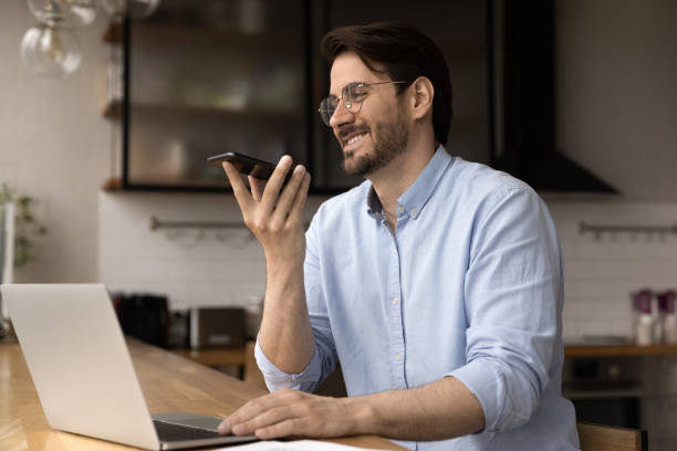 l'uomo sorridente registra un messaggio audio su smartphone - mid adult audio foto e immagini stock