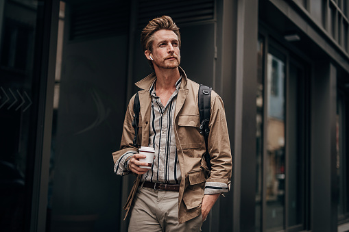 One man, handsome young man on the street outdoors in city, holding disposable cup of coffee.