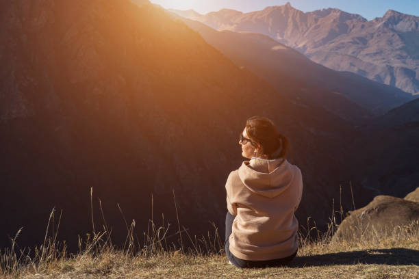 istock Brunette sits on brown grass edge looking at hill landscape 1292936571