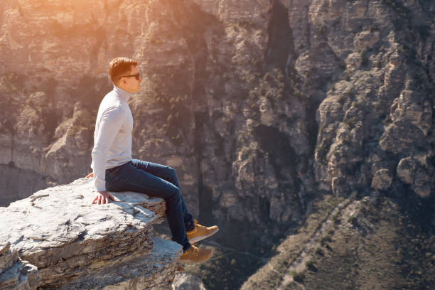 istock Excited guy sits on edge of large grey rock against cliffs 1292936596