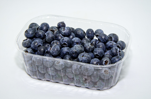 Fresh organic blueberries in a transparent plastic packaging on a white background. Seasonal natural vitamines and antioxidants. Healthy diet and nutrition concept.