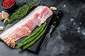 Raw sliced pork bacon ready for cooking. Black background. Top view. Copy space