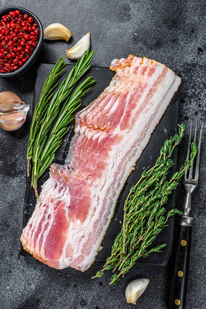 istock Raw sliced pork bacon ready for cooking. Black background. Top view 1292944382