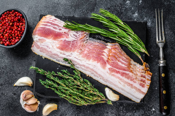 istock Raw sliced pork bacon ready for cooking. Black background. Top view 1292944386