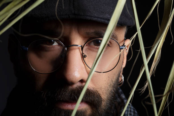Portrait of handsome charismatic man looking towards camera through tree leaves.