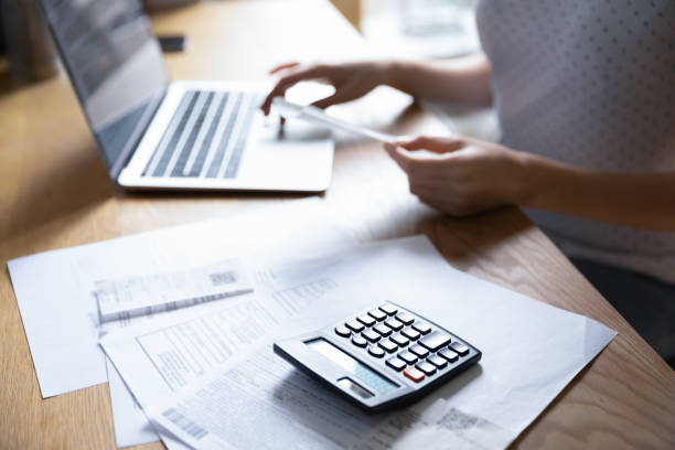 istock Close up young woman calculating bills, using laptop, holding document 1292945431