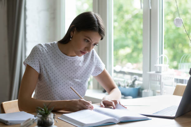 istock Focused woman studying, writing notes, sitting at desk with laptop 1292945441