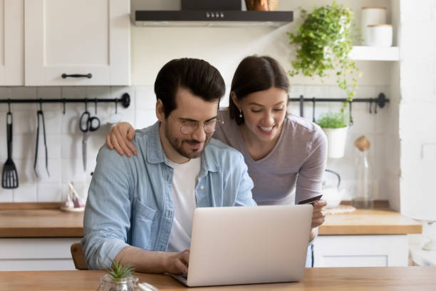 glückliches paar mit laptop in der küche, machen internet-zahlung - wallet couple stock-fotos und bilder