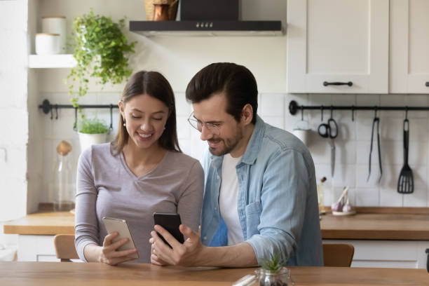istock Happy young couple using smartphones, sitting at table in kitchen 1292945773