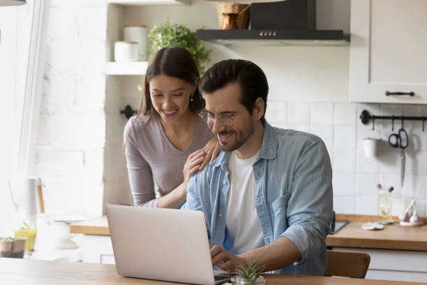 istock Happy young couple using laptop in modern kitchen together 1292945775