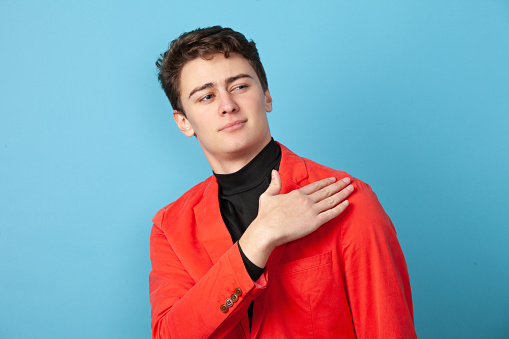 Close-up studio portrait of 18 year old man in pink jacket on blue background