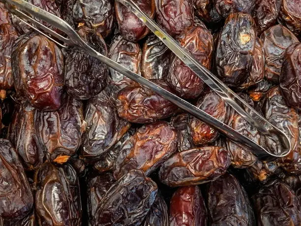 Photo of Dried date fruits on sale and metal forceps at a market or store