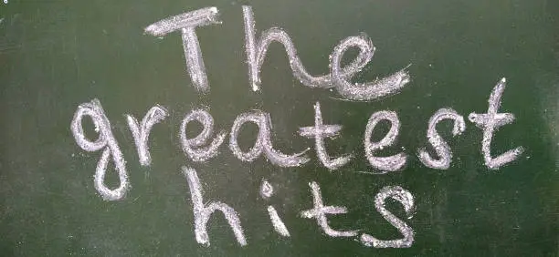 Photo of The phrase The greatest hits is handwritten in white chalk on a dark green blackboard.