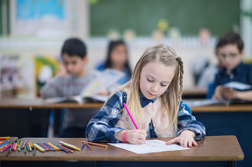 A Caucasian elementary school girl is busy writing on her notebook in class.