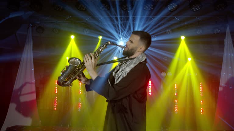 Live performance of saxophonist man with saxophone, dancing on concert musician stage with lights