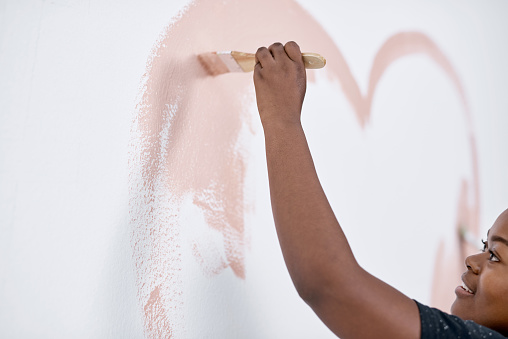 Shot of a young woman painting a heart on a wall