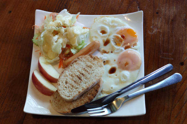 Overhead view of homemade breakfast, freshness warm fried egg, sausage, salad and toast serving on white plate on wooden table, Englisches, amerikanisches Frühstück