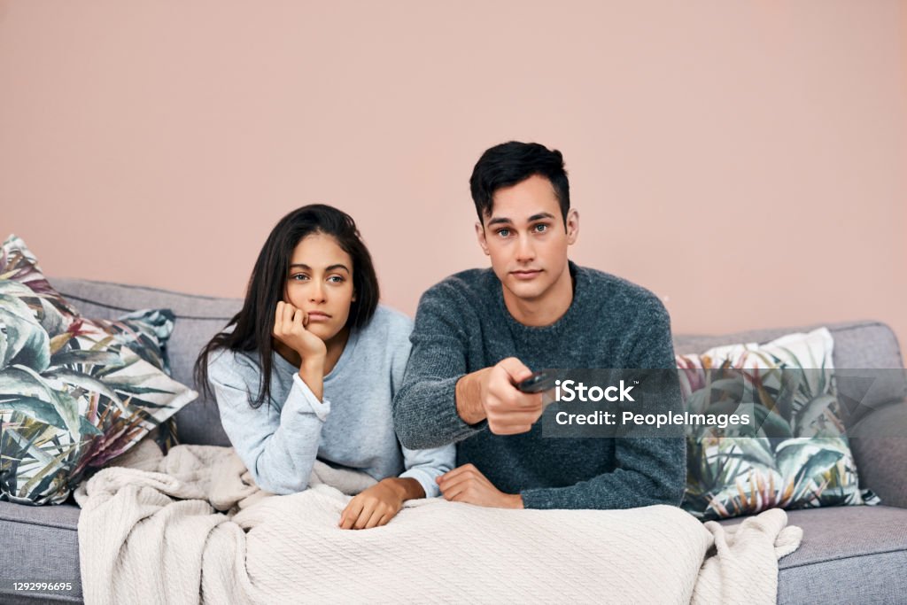 Some breaking news will clear that boredom right up Shot of a young couple watching tv while recovering from an illness at home Couple - Relationship Stock Photo