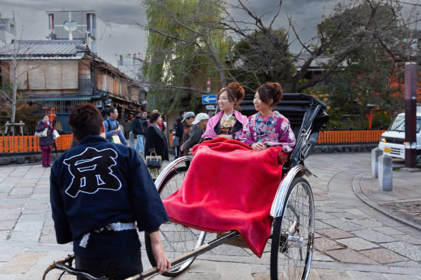 Kyoto, Japan - December 8, 2012: Two Japanese woman dressed as Geisha enjoying weekend travelling by rickshaw (Jinrikisha) around Arashiyama tourist district in Kyoto, Japan.