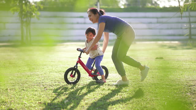 4K Asian mother teaching son to riding a bicycle in park.