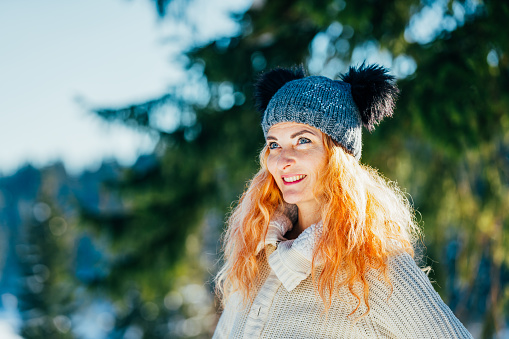 Beautiful happy woman at snowcapped meadow near forest in winter time.