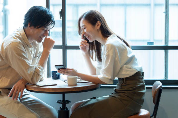 カフェで笑顔で楽しい会話をしているカップル - スマホ 日本人 ストックフォトと画像
