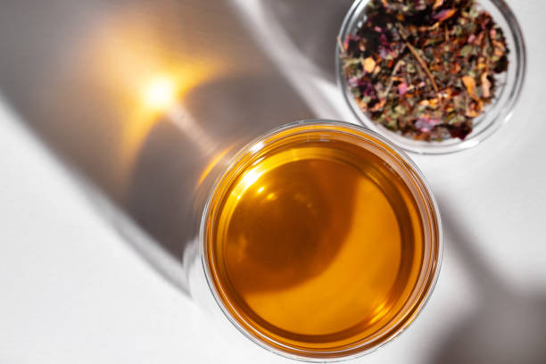 Glass cup of tea and dry tea leaves on white table