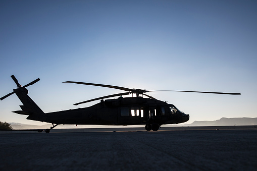 Silhouette of a military helicopter flying during sunset.