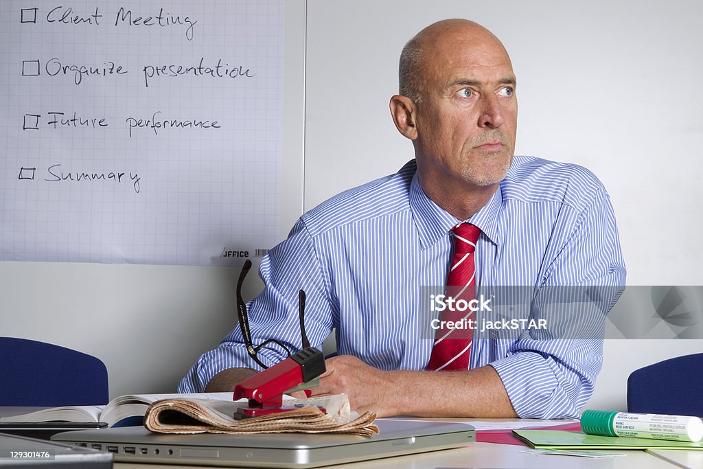 Biznesmen siedzi przy biurku w biurze. - Zbiór zdjęć royalty-free (Biuro)