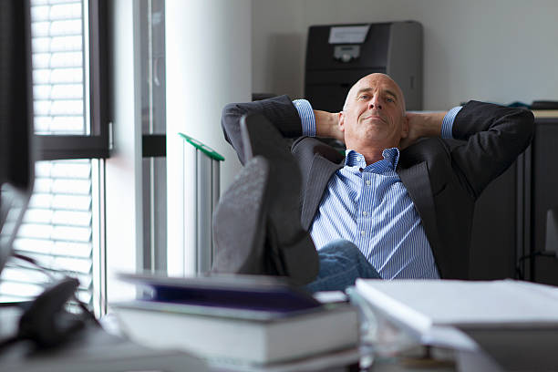 homme d'affaires de détente avec les pieds sur le bureau - hands behind head photos et images de collection