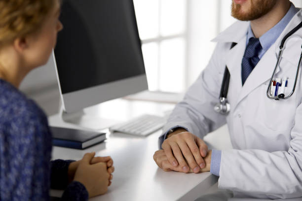 istock Unknown red-bearded doctor and patient woman discussing current health examination while sitting in sunny clinic, close-up. Medicine concept 1293016468