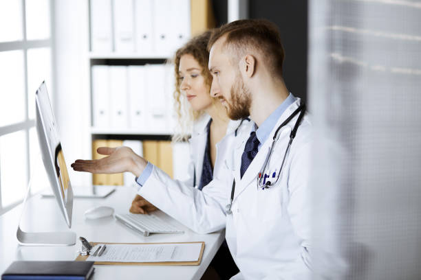istock Red-bearded doctor with female colleague discussing current disease therapy while sitting at working place in clinic. Team work in medicine 1293016483