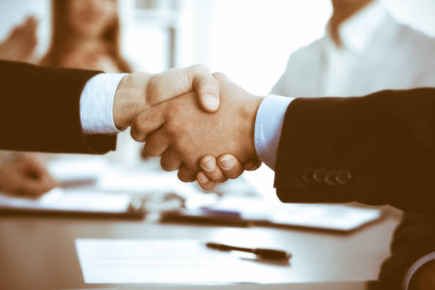 istock Business people shaking hands at meeting while theirs colleagues clapping and applauding. Group of unknown businessmen and women in modern white office. Success teamwork, partnership and handshake concept 1293018928