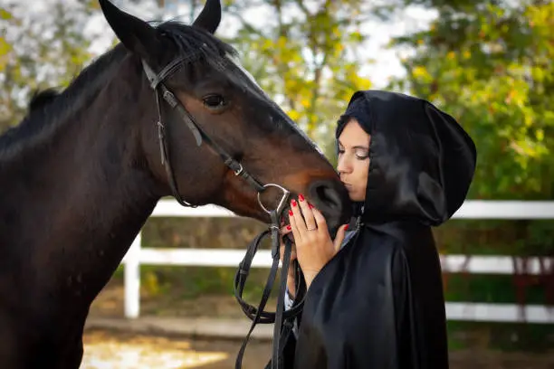 Photo of Girl in a black cloak hugs and kisses a horse