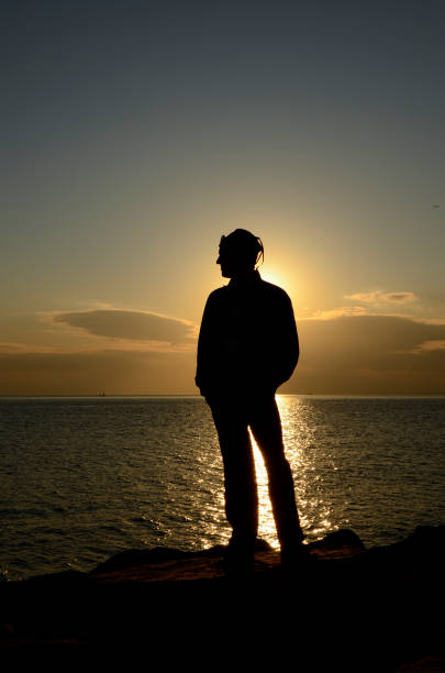 istock Silhouette Young man on the rocks at sunset on the beach, alone 1293027856