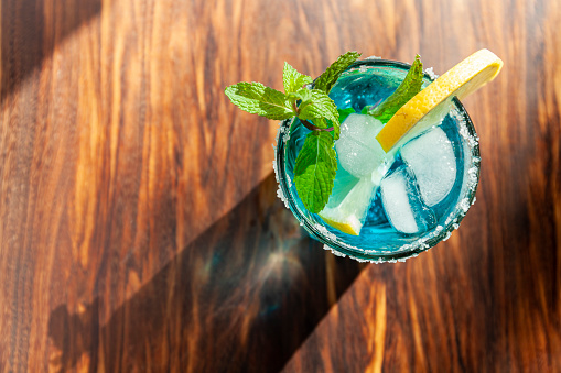 Blue alcoholic cocktail in a glass on a wooden bar counter. Stock photo