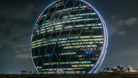 The Aldar headquarters building night timelapse is the first circular building of its kind in the Middle East in Abu Dhabi, UAE. Cloudy sky