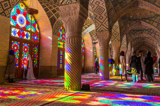 Lots of tourists taking photos in the interior of Nasir Al-Mulk Mosque (Pink Mosque) with colorful shining stained glass windows. stock photo