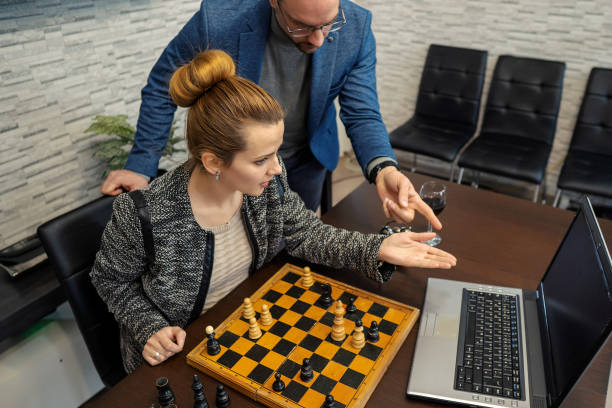 femme d’affaires jouent aux échecs avec un instructeur masculin - chess board room business strategy photos et images de collection