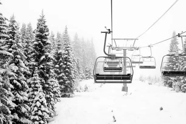 Black and white image of snow covered spruce trees and ski lift along a ski slope at Hafjell ski resort (near Lillehammer) in Norway on a cloudy day with snowfall in late January.