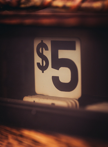 Five dollar label showing on an antique cash register with warm tones.
