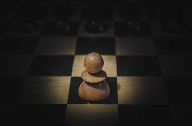 istock Chess figures on a board with single white pawn in a spotlight 1293052505