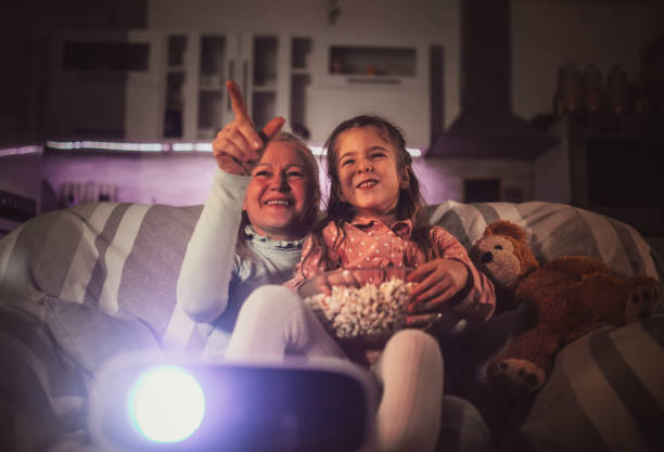 Grandma and grandchild watching projector movies with popcorn in evening at home stock Grandma and grandchild watching projector movies with popcorn in evening at home stock popcorn snack bowl isolated stock pictures, royalty-free photos & images