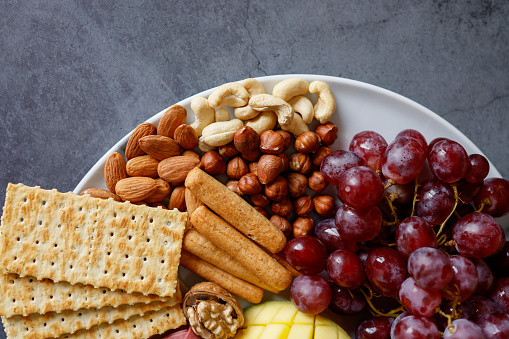 Istanbul, Turkey-December 24, 2020: Nuts, Grapes, Crackers and Waffles on Plate on Dark Gray Concrete Background, Healthy Breakfast Trend in Social Media, Full Frame, Studio Shot, Flat lay.