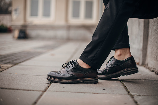 One man, modern young man in leather shoes, sitting on the street in city.