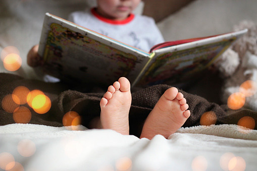 feet of a child reading a book under a blanket in christmas lights