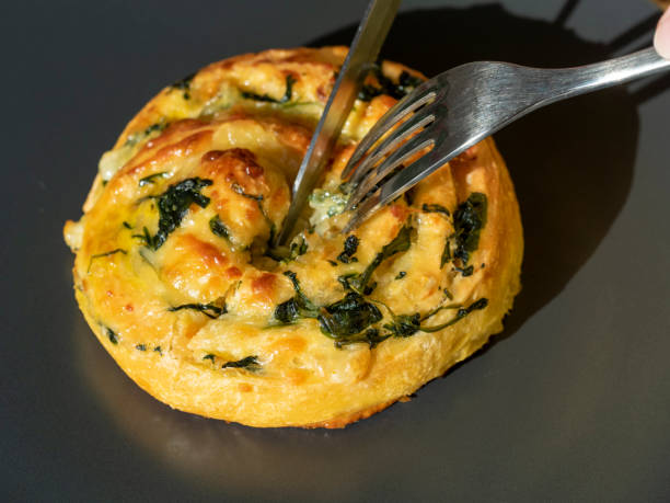 a curl of dough with spinach and cheese is cut with a knife and fork. Side view, close-up