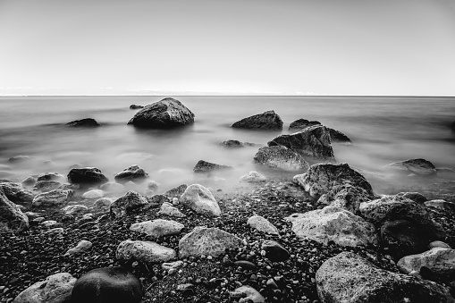Long exposure black and white photo of rocks and waves by the sea