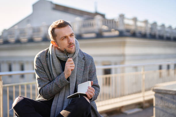 istock Young man sitting on a roof and thinking, holding notes 1293082439