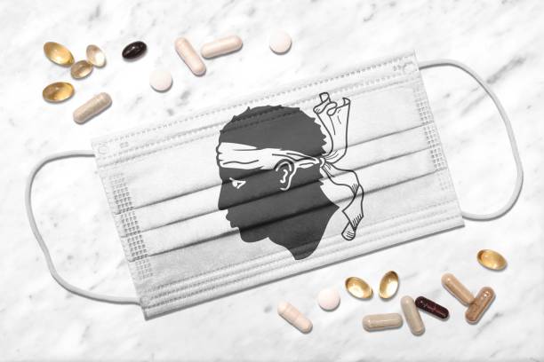 Face mask with flag of Corsica during coronavirus pandemic Face mask showing colors of the flag of Corsica during coronavirus pandemic surrounded by pills corsican flag stock pictures, royalty-free photos & images